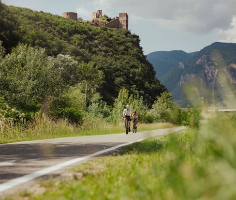 Ciclisti sulla ciclabile di fondovalle sotto le rovine di un castello in Alto Adige